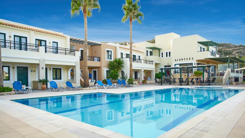 a swimming pool in front of a building with palm trees at Dionysos Apartments & Studios in Stalida