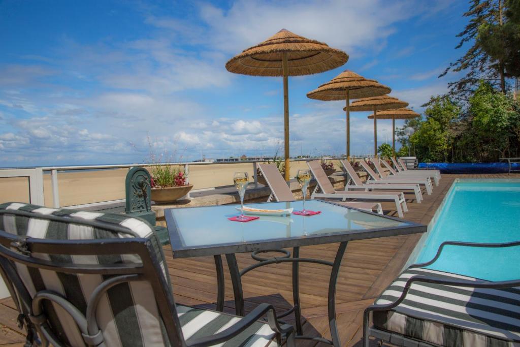 einen Tisch und Stühle mit Sonnenschirmen neben einem Pool in der Unterkunft Arc Hôtel Sur Mer in Arcachon