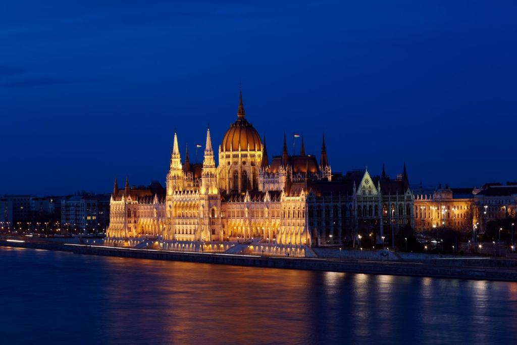 a parliament building lit up at night next to the water at Boutique Hotel Victoria Budapest in Budapest