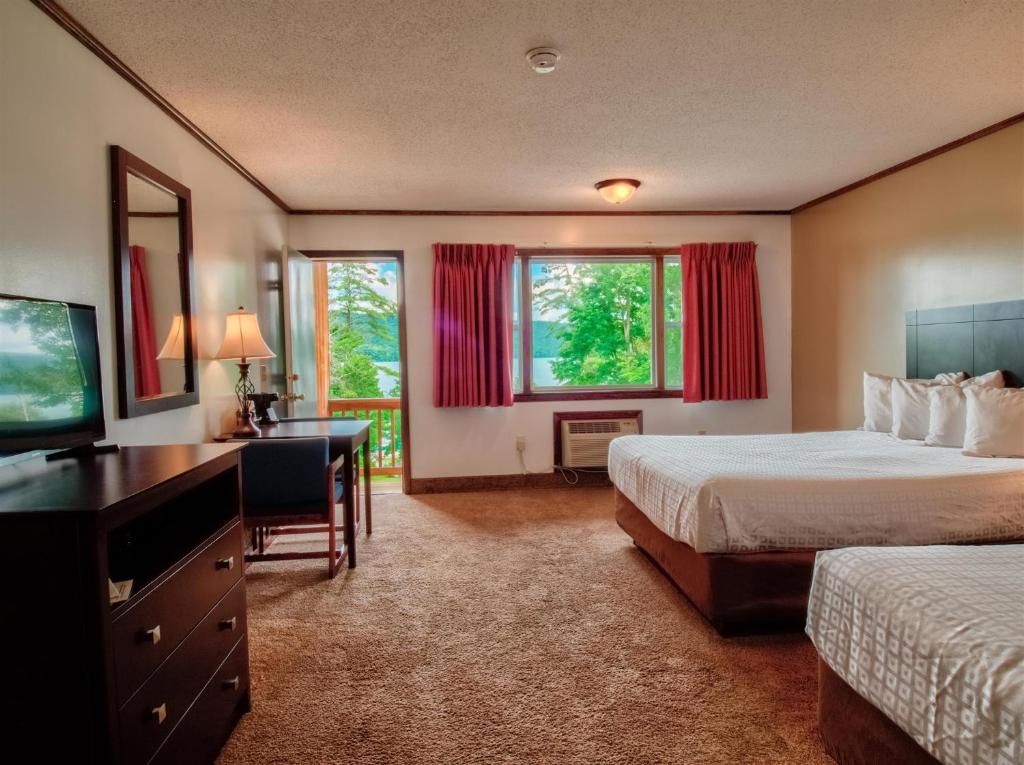 um quarto de hotel com duas camas e uma secretária e uma televisão em Lake 'N Pines Motel em Cooperstown