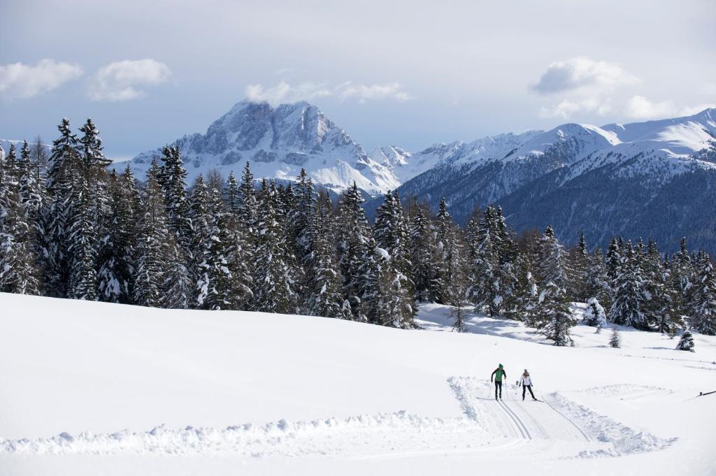 two people skiing down a snow covered slope with mountains at Hotel Tirolerhof in Rodengo