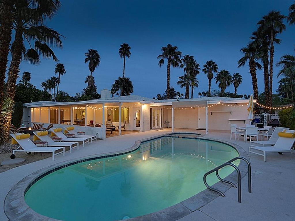 a swimming pool with chairs and a house with palm trees at Shooting Star Permit# 3210 in Palm Springs