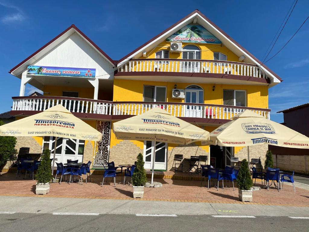 a yellow building with tables and umbrellas in front of it at Motel California in Mărtineşti