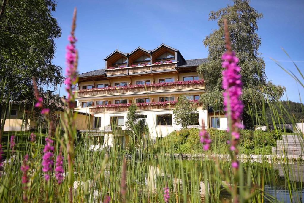 a building with pink flowers in front of a pond at Hotel garni Kranzbichlhof in Dürrnberg