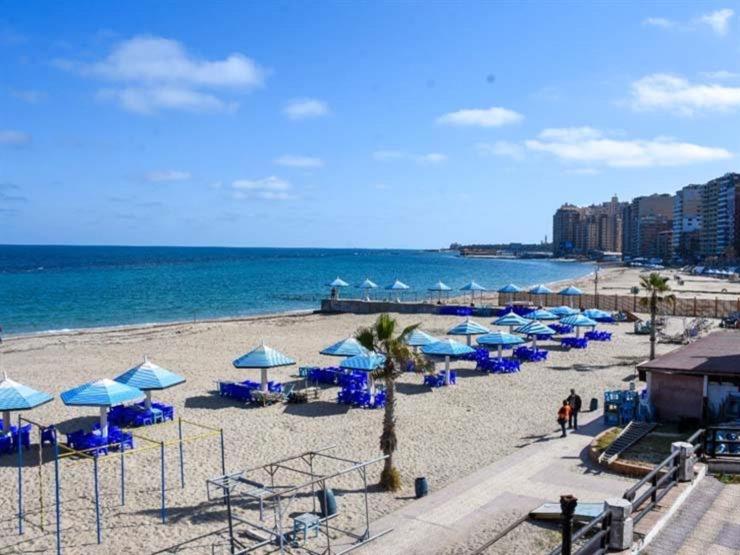 einen Strand mit blauen Sonnenschirmen und dem Meer in der Unterkunft the flowers apartment in Alexandria