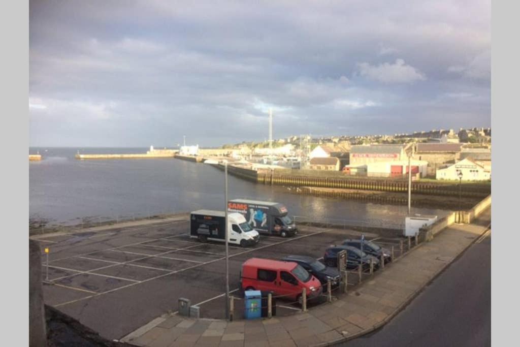 a parking lot with cars parked next to the water at Centrally located 1 bed modern flat with harbour views in Wick