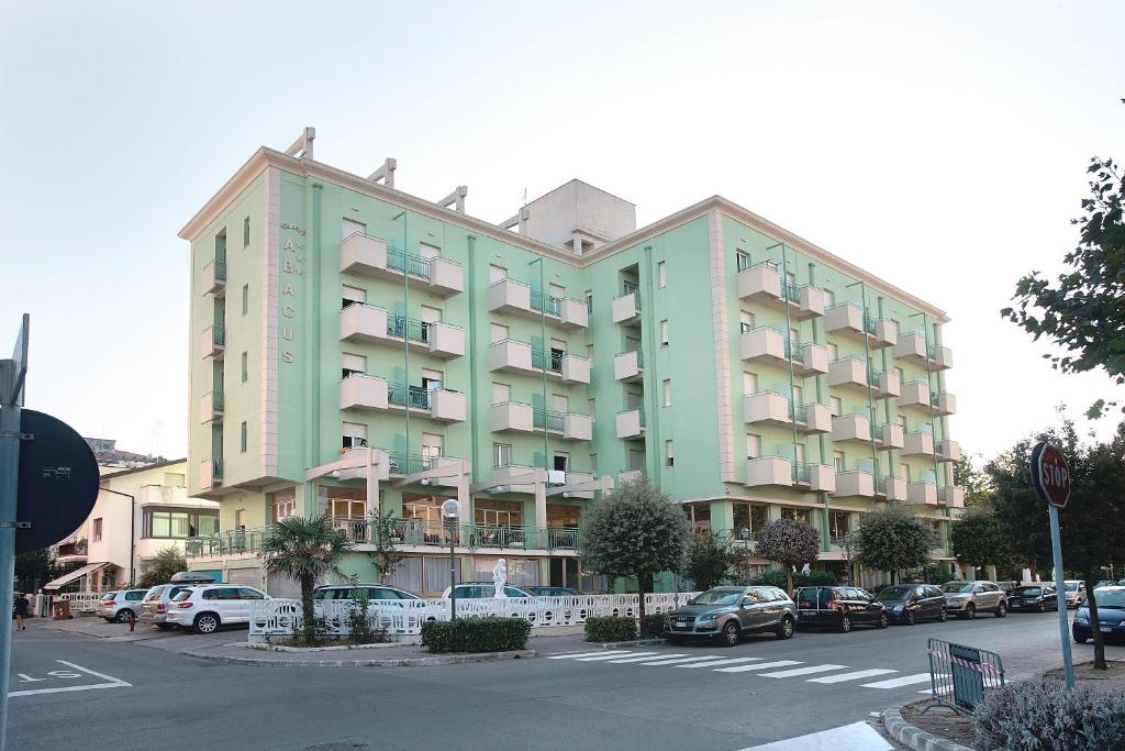 a large green building with cars parked in a parking lot at Hotel Abacus in Cesenatico