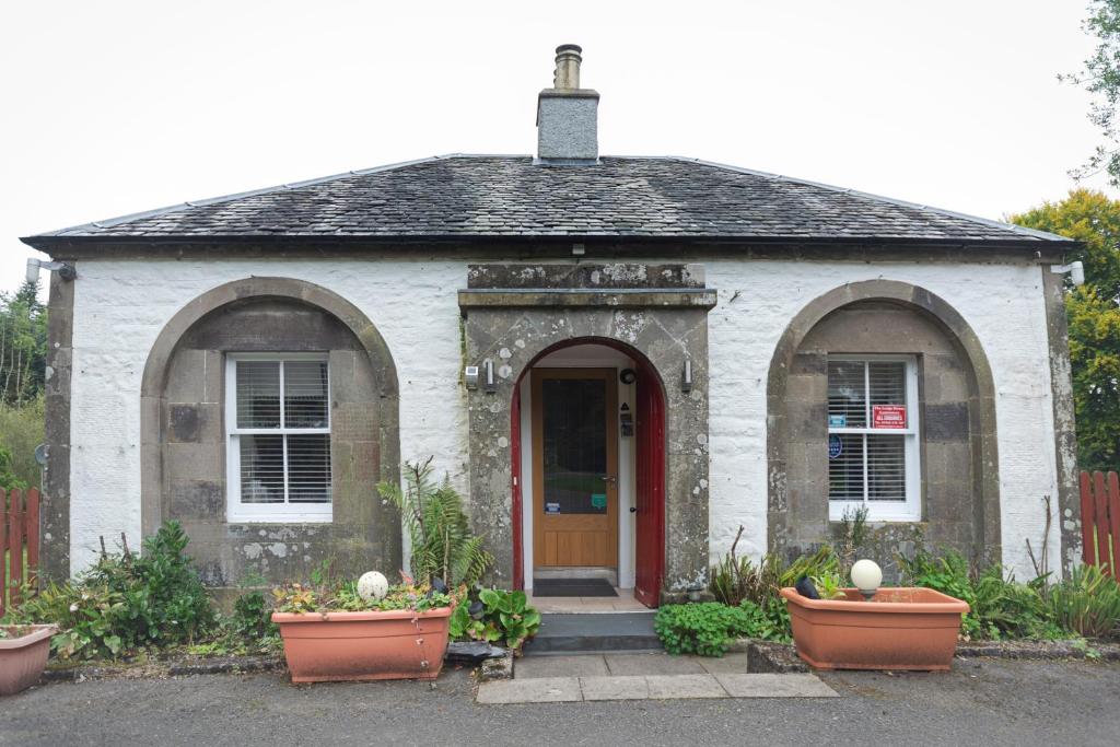 The Lodge House Callander في كالالندر: منزل أبيض صغير مع باب احمر