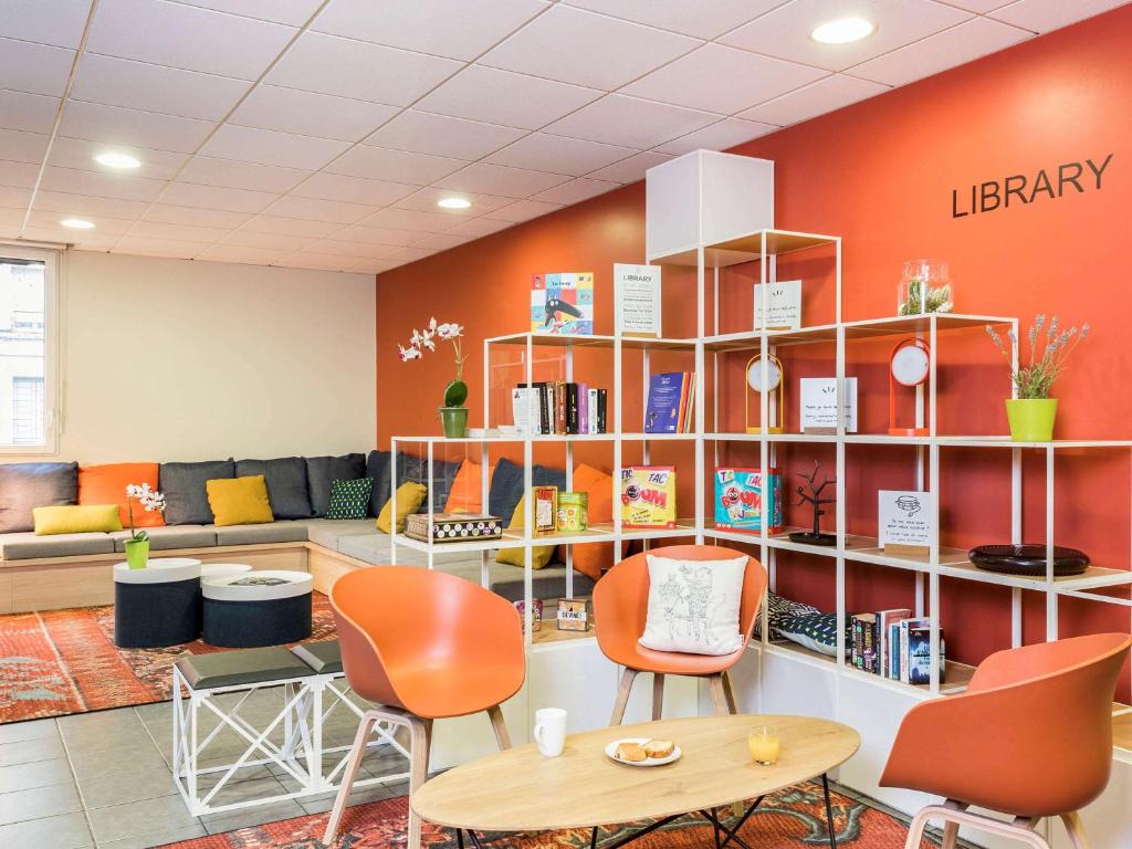 - une bibliothèque avec des murs orange, des chaises et une table dans l'établissement Aparthotel Adagio Access Paris Asnières, à Asnières-sur-Seine