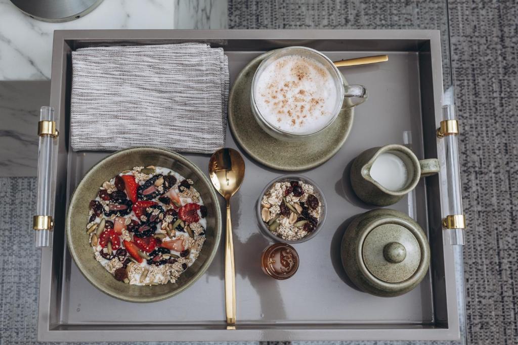 A breakfast tray arranged with yogurt, fruit, granola, coffee, and milk.