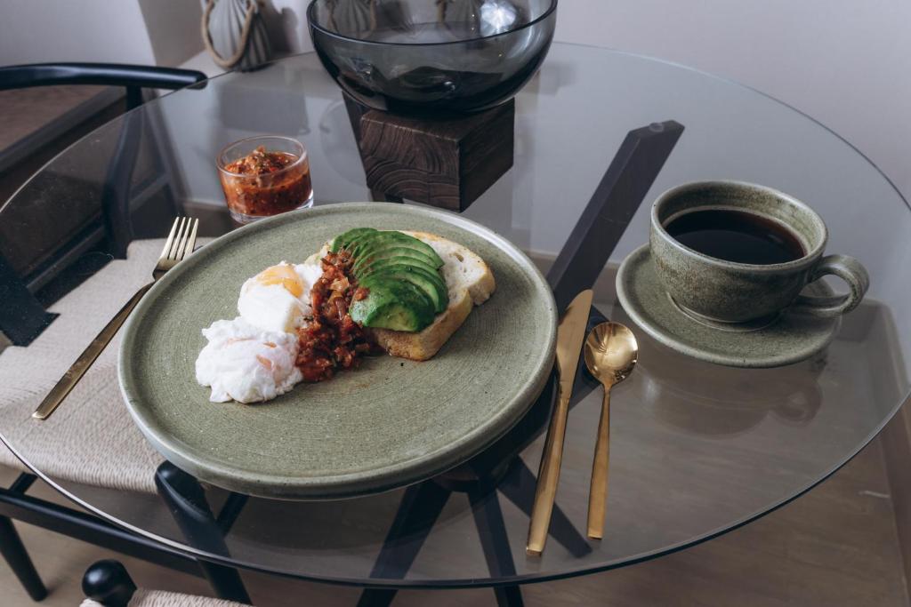 A breakfast plate with avocado toast, eggs, spicy relish, and coffee.