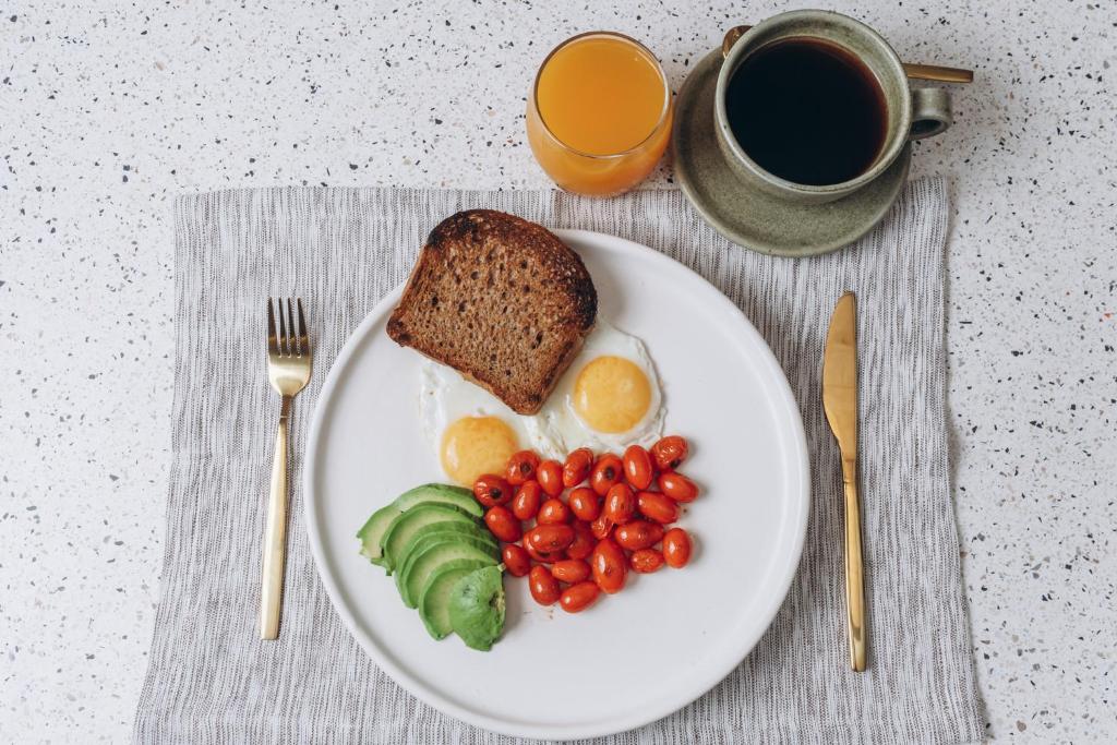 A simple breakfast plate with toast, eggs, tomatoes, avocado, coffee, and juice.