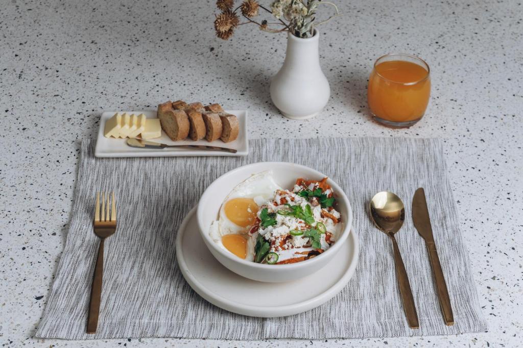 A plated egg breakfast with greens, bread, fruit, and orange juice.