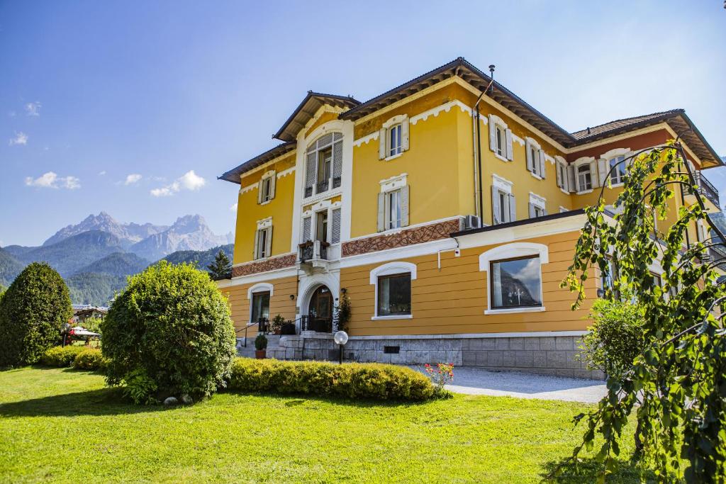 een geel huis met bergen op de achtergrond bij Hotel Villa Imperina in Agordo