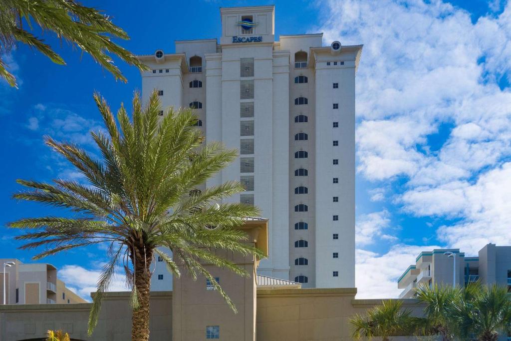 a large white building with a palm tree in front of it at Escapes! To The Shores Orange Beach, A Ramada by Wyndham in Orange Beach