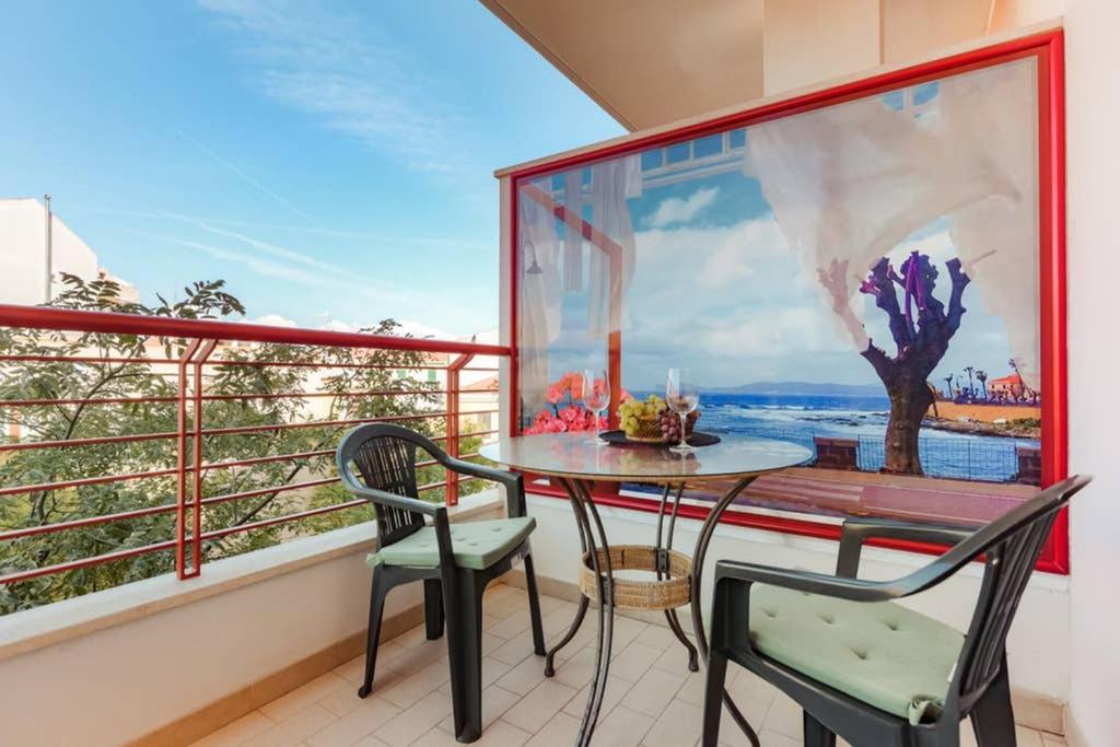 balcón con mesa, 2 sillas y ventana en Delizioso appartamento ad Alghero, en Alghero