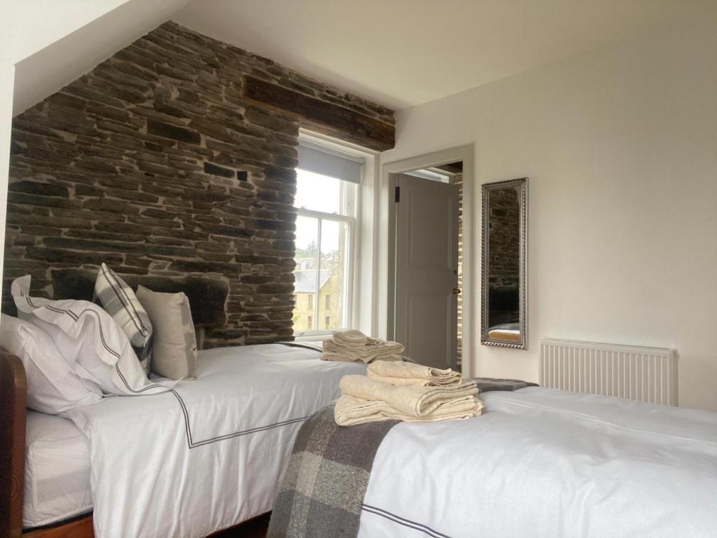 2 camas blancas en una habitación con una pared de ladrillo en Manor House Hotel, en Thurso