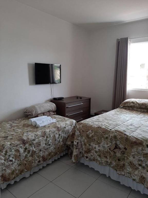a bedroom with two beds and a tv on the wall at Hospedaria Nossa Casa in Braço do Norte