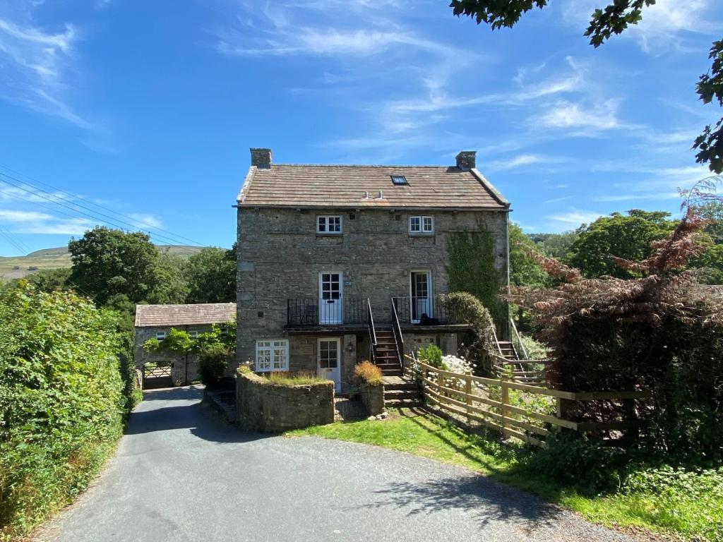 een oud stenen huis aan de kant van een weg bij Wonderfully Scenic and Comfortable Dales Mill Property in West Burton
