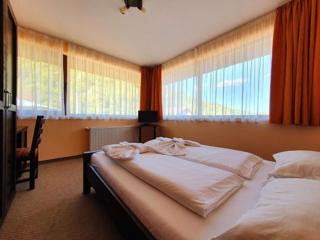 Schlafzimmer mit einem Bett mit weißer Bettwäsche und Fenstern in der Unterkunft Family Hotel Chiflik Hills in Chiflik