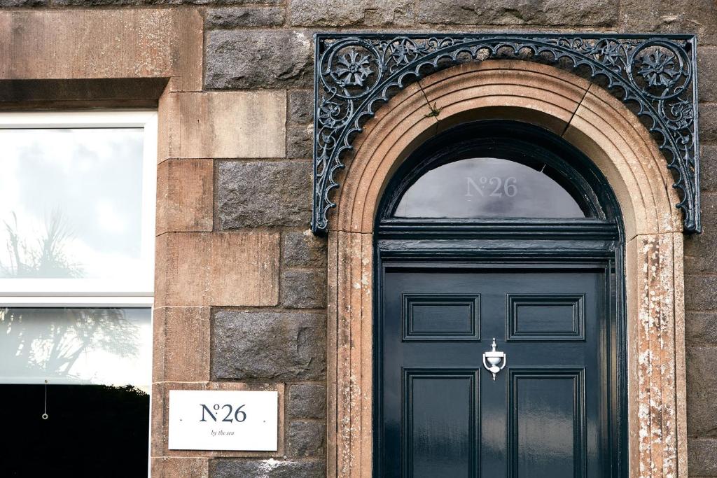 a black door on a brick building with a sign above it at No.26 By The Sea in Oban