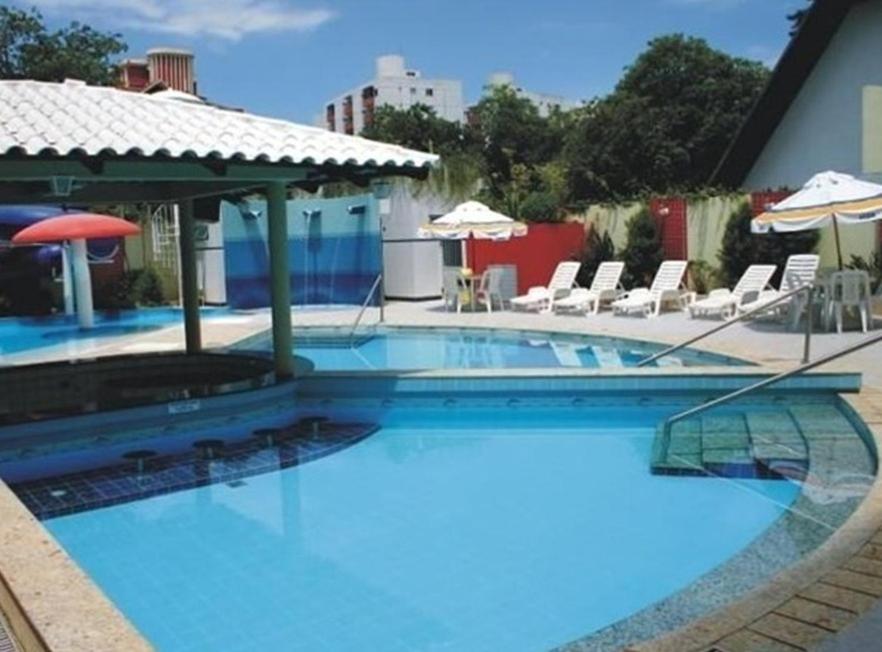 a large swimming pool with chairs and an umbrella at Hot Star Thermas Hotel - NO CENTRO DE CALDAS NOVAS in Caldas Novas