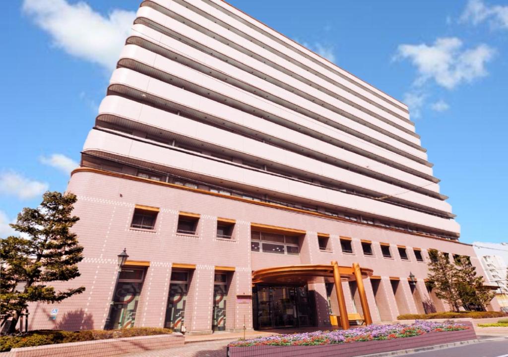 a tall white building with a tree in front of it at U-Community Hotel in Osaka