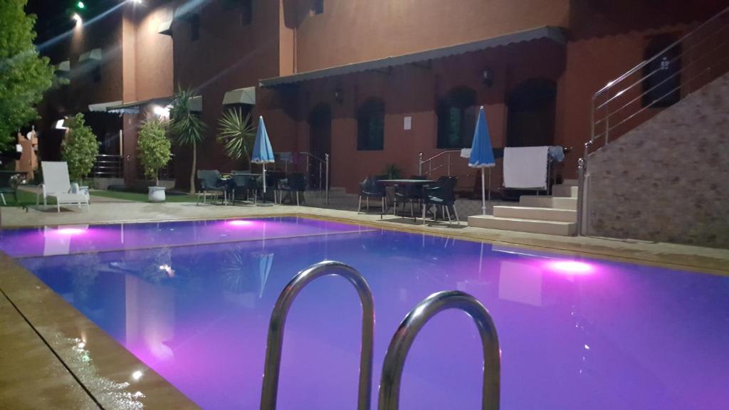 Hôtel Ajil Cascades D'ouzoud في أوزود: حمام سباحة في الليل مع أضواء أرجوانية