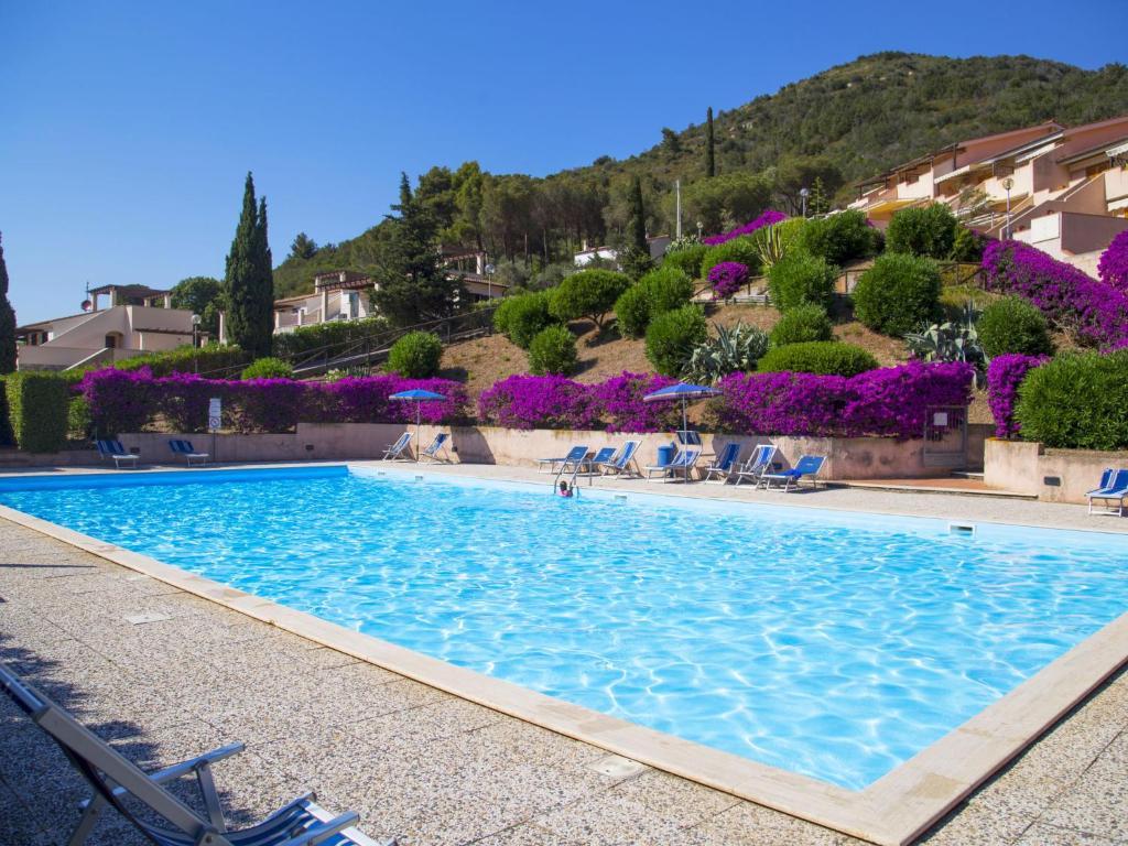 a large swimming pool with chairs and purple flowers at Apartment Terrazza Cala Rossa by Interhome in Nisporto