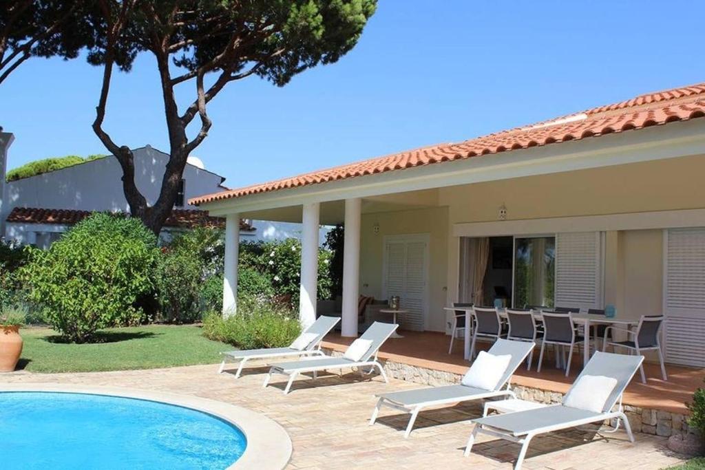 a villa with a swimming pool and chairs next to a house at Villa Quadradinhos 46Q Located close to the tennis courts and just 100m from the famous Restaurant in Vale do Lobo