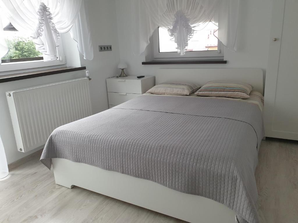 a white bed in a bedroom with two windows at Wypoczynek Pod Lasem in Kudowa-Zdrój