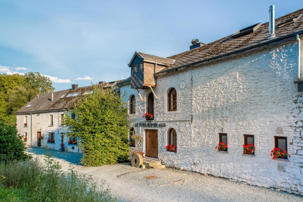 an old stone building with red flowers on the windows at Le Moulin d'en Bas in Saint-Hubert