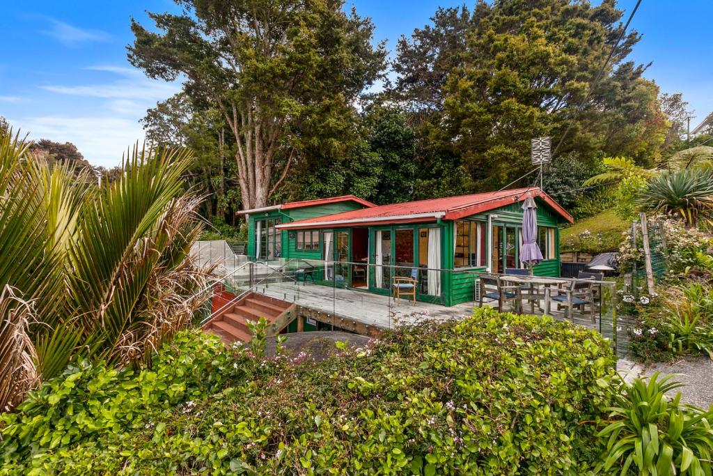 a green house with a red roof in a garden at Pohutukawa Cottage - Matakana Holiday Home in Tawharanui