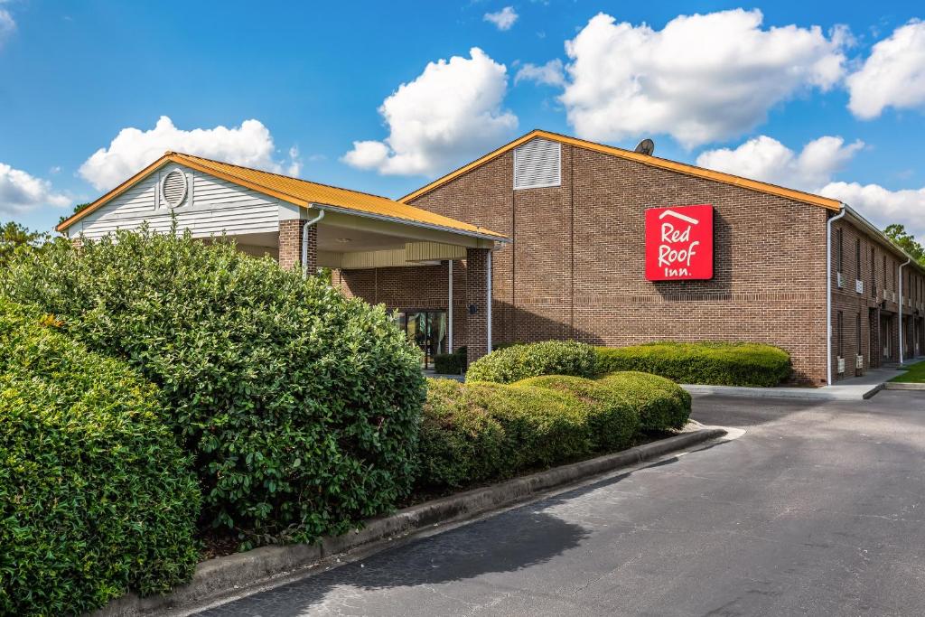 a red sign on the side of a building with bushes at Red Roof Inn Hardeeville in Hardeeville