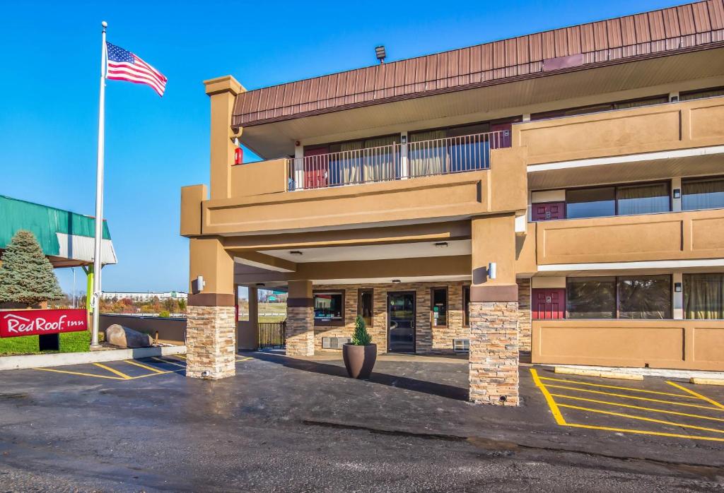 Red Roof Inn Cincinnati Airport–Florence/ Erlanger في إيرلانغر: مبنى مع العلم الامريكي في مواقف السيارات