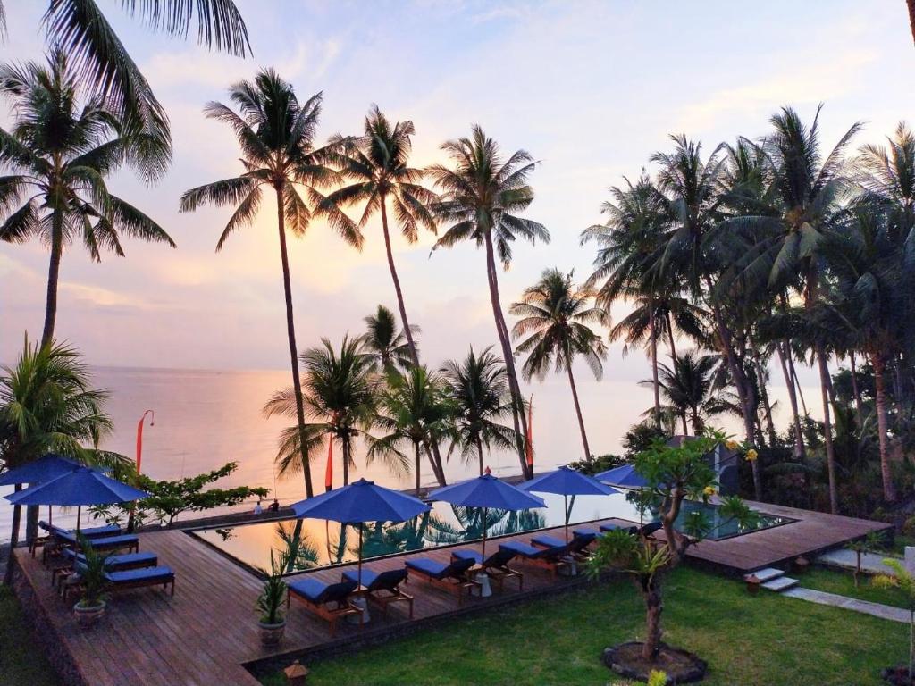 a resort with palm trees and a pool with blue umbrellas at The Kirana Tembok in Tejakula