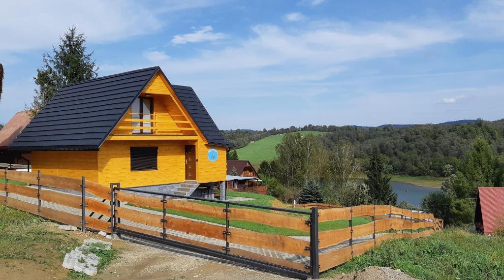 a yellow house with a black roof on top of a fence at Willa Kotwica - Solina Chrewt in Chrewt