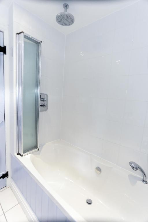 a white bathroom with a tub and a shower at Linden House in West Wittering