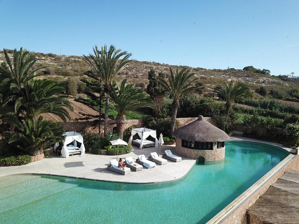 a pool with chairs and a gazebo and palm trees at La Sultana Oualidia in Oualidia