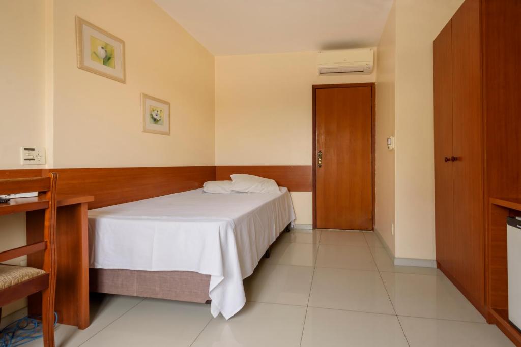 a bedroom with a white bed and a wooden door at Plaza Suite Hotel in Taubaté