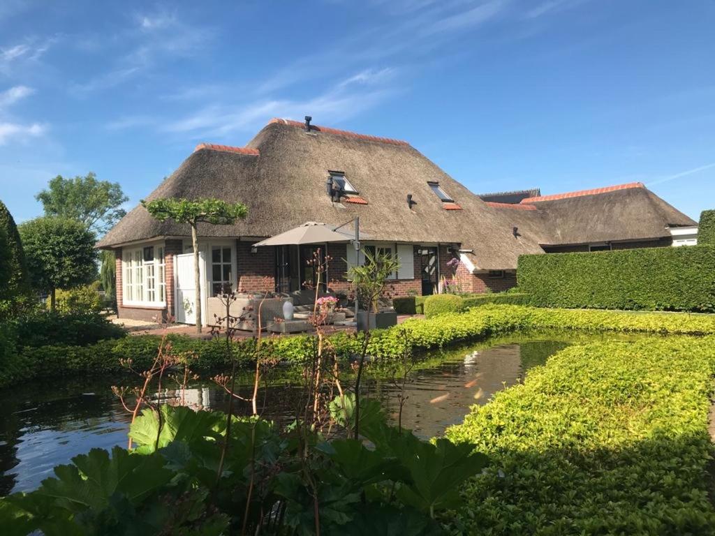 ein strohgedecktes Haus mit einem Teich davor in der Unterkunft De Tuinkamer in Ter Apel