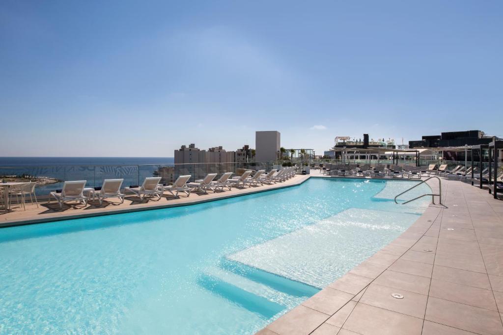 a large swimming pool with lounge chairs on top of a building at be.HOTEL in St Julian's