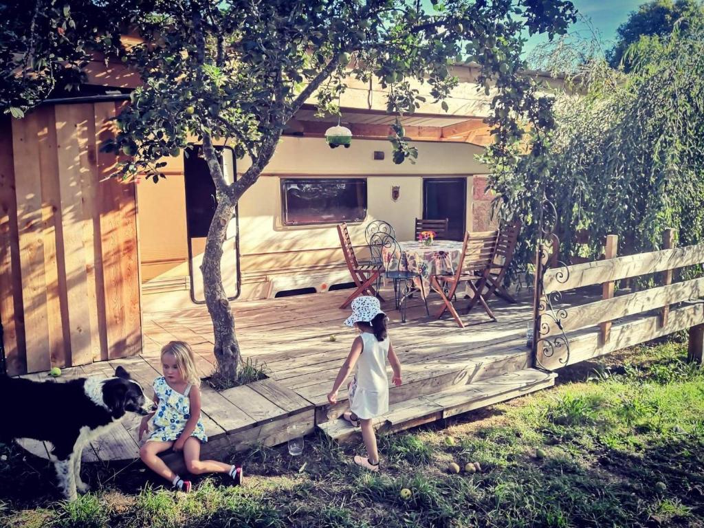 dos niñas de pie en una terraza de madera con un perro en caradjango , caravane chauffée et climatisée, en Lupersat