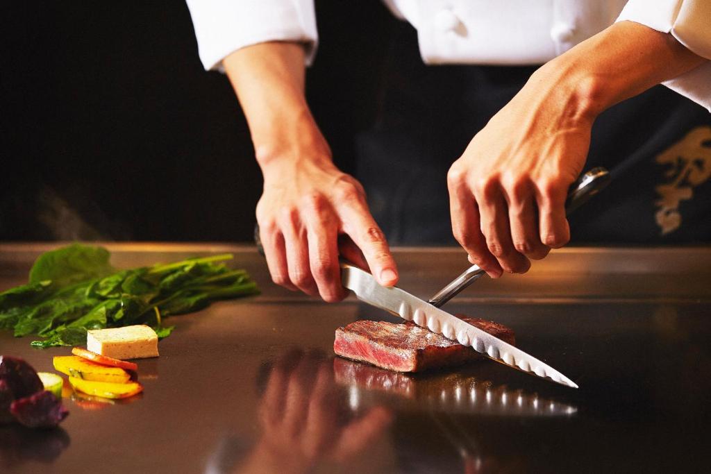 a person cutting meat with a knife on a counter at ANA InterContinental Manza Beach Resort by IHG in Onna
