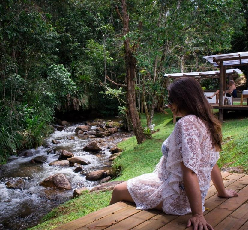 a woman sitting on a wooden bridge next to a stream at Pousada Vila Santa Barbara in São Francisco Xavier