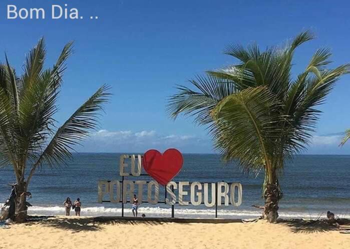 a sign on a beach with palm trees and the ocean at Condomínio Praia dos Corais 1 in Coroa Vermelha