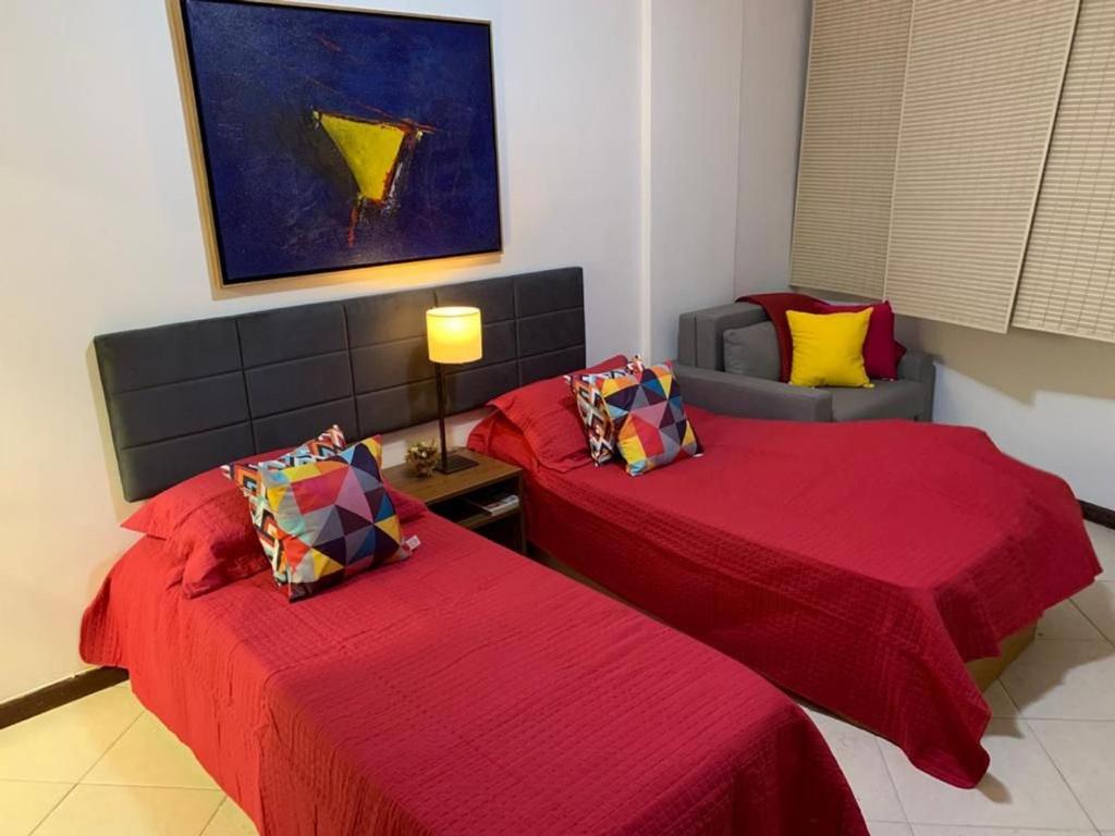 a room with two beds with red sheets and a couch at COPACABANA - ÓTIMA LOCALIZAÇÃO in Rio de Janeiro