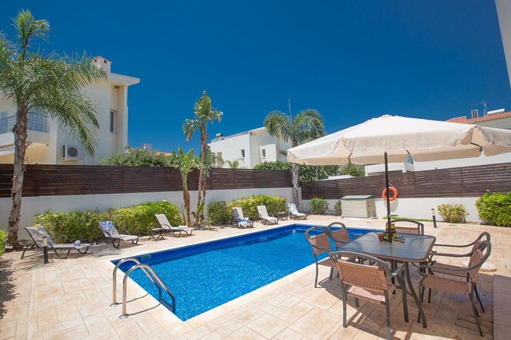 a pool with chairs and a table and an umbrella at Villa Dafnis Chrysos - Modern 3 Bedroom Protaras Villa with Pool - Close to Fig Tree Bay Beach in Protaras