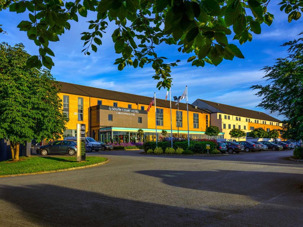 ein großes gelbes Gebäude mit Autos auf einem Parkplatz in der Unterkunft Great National South Court Hotel in Limerick