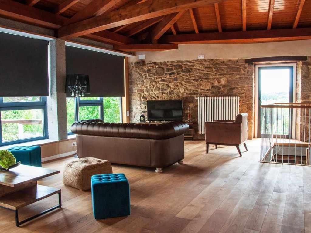 - un grand salon avec un canapé en cuir et un mur en pierre dans l'établissement O Forno Casa Ferrador Ribeira Sacra, à Sober